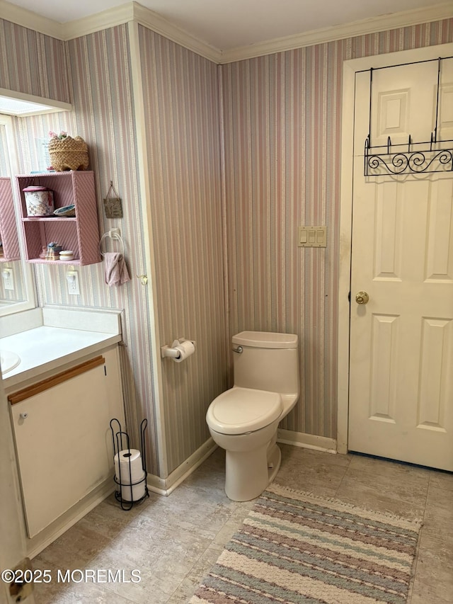 bathroom with crown molding, wallpapered walls, baseboards, toilet, and vanity