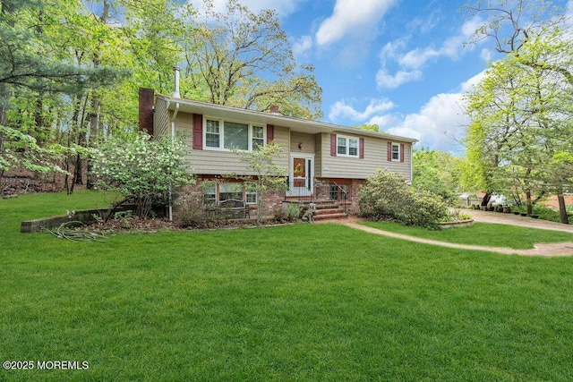 split foyer home featuring a chimney, brick siding, and a front lawn