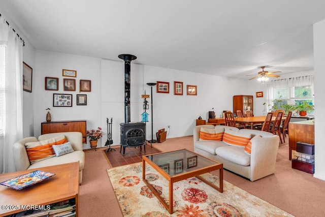 carpeted living area with a wood stove and a ceiling fan