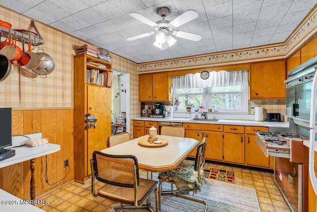 kitchen with a sink, light countertops, stainless steel gas stove, wallpapered walls, and brown cabinetry