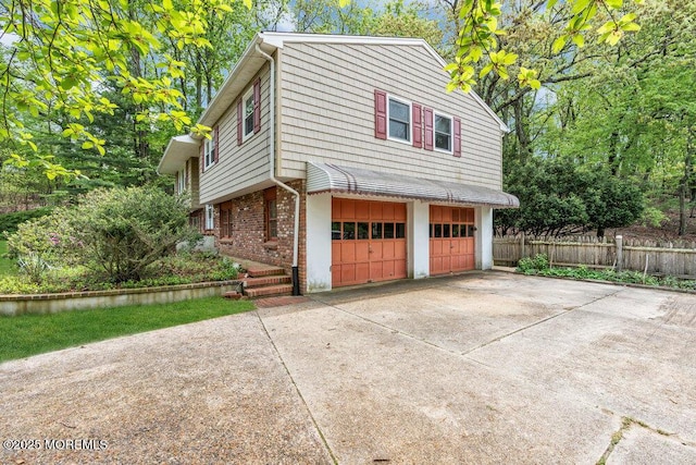 view of side of home featuring fence, brick siding, an attached garage, and concrete driveway