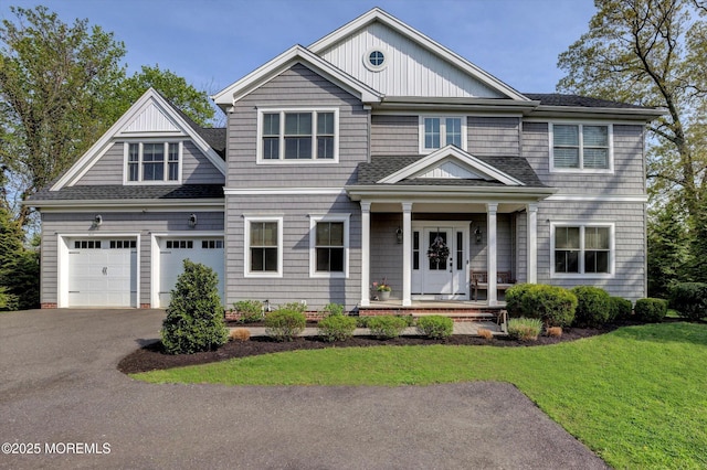 craftsman-style home featuring roof with shingles, driveway, a front yard, and covered porch