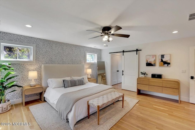 bedroom with visible vents, baseboards, recessed lighting, a barn door, and light wood-style flooring