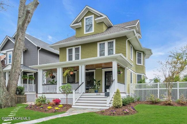 traditional style home with a porch, fence, a shingled roof, and a front yard