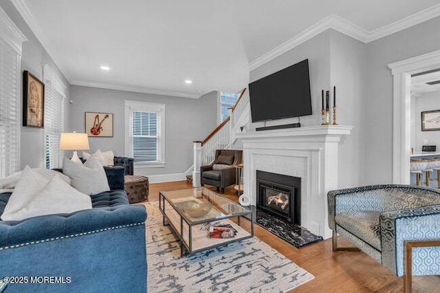 living area with a glass covered fireplace, crown molding, recessed lighting, and wood finished floors
