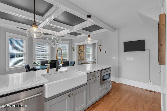 kitchen with pendant lighting, appliances with stainless steel finishes, a sink, baseboards, and a notable chandelier