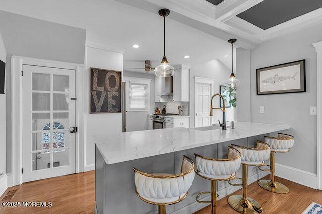 kitchen with stainless steel range with gas stovetop, a sink, light wood-style flooring, and wall chimney exhaust hood