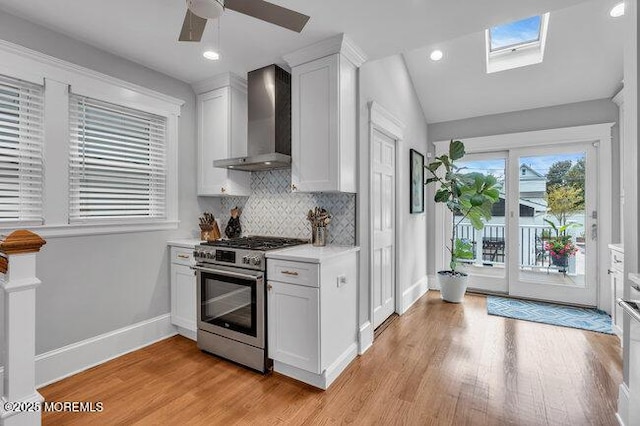 kitchen featuring light countertops, gas range, light wood-style flooring, wall chimney exhaust hood, and tasteful backsplash