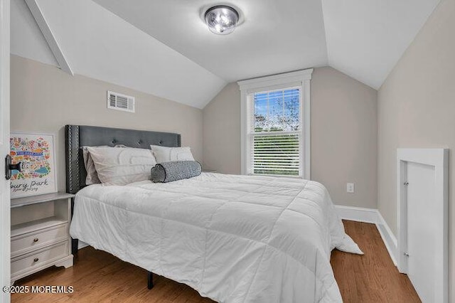 bedroom with baseboards, visible vents, wood finished floors, and lofted ceiling