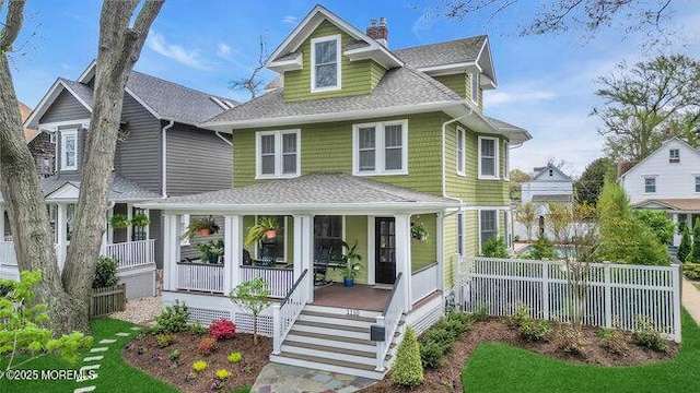 american foursquare style home featuring a porch, roof with shingles, fence, and a chimney