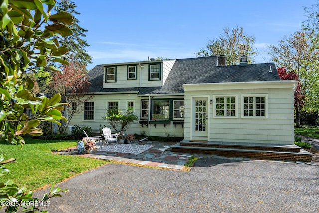 view of front of house featuring a shingled roof, a patio area, and a front yard