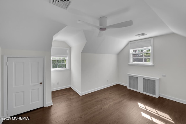 additional living space featuring visible vents, dark wood-type flooring, radiator heating unit, and vaulted ceiling