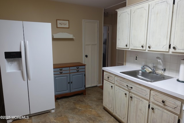 kitchen with light countertops, tasteful backsplash, white refrigerator with ice dispenser, and a sink