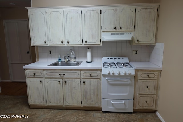 kitchen featuring under cabinet range hood, baseboards, white gas range oven, a sink, and decorative backsplash