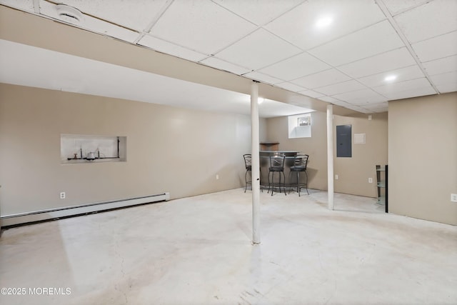 finished below grade area featuring a drop ceiling, a baseboard heating unit, and electric panel