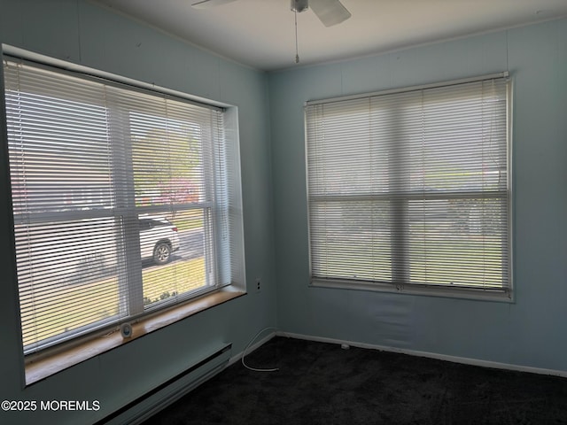 unfurnished room featuring baseboard heating, ceiling fan, dark carpet, and a healthy amount of sunlight