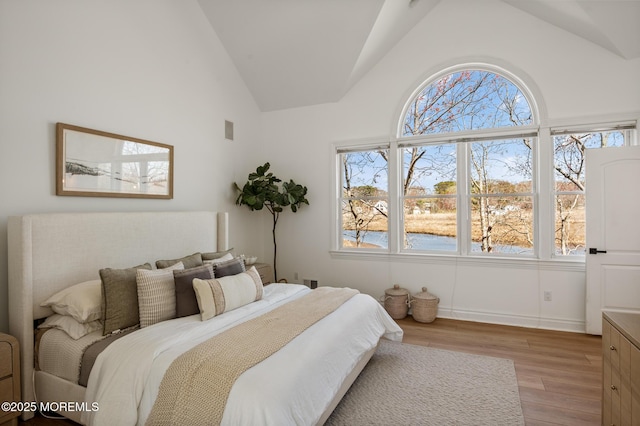 bedroom with visible vents, light wood-style floors, high vaulted ceiling, and a water view