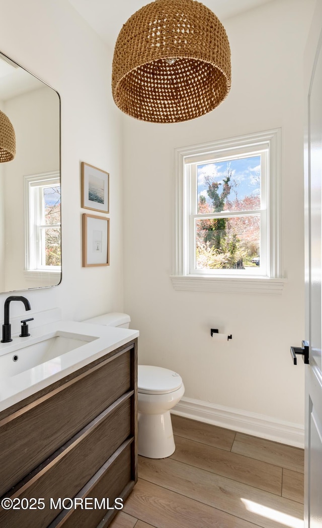 bathroom with baseboards, wood finished floors, toilet, and vanity