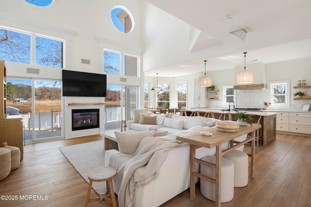 living area featuring a glass covered fireplace, a high ceiling, plenty of natural light, and light wood-style floors