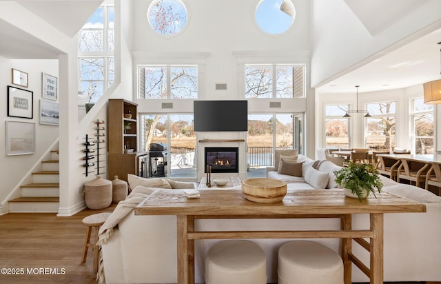 living area featuring a glass covered fireplace, stairs, a towering ceiling, wood finished floors, and plenty of natural light