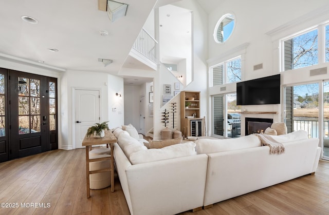 living area featuring a towering ceiling, a glass covered fireplace, and light wood-style floors