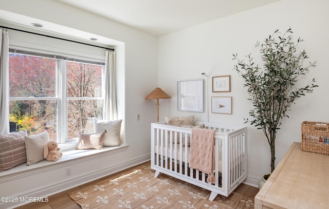 bedroom with a nursery area, wood finished floors, and baseboards