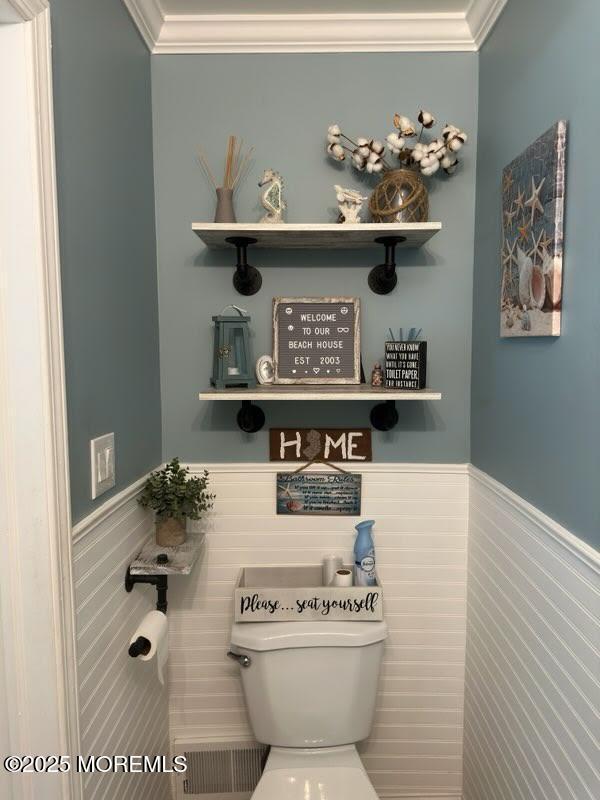 bathroom featuring toilet, ornamental molding, and a wainscoted wall