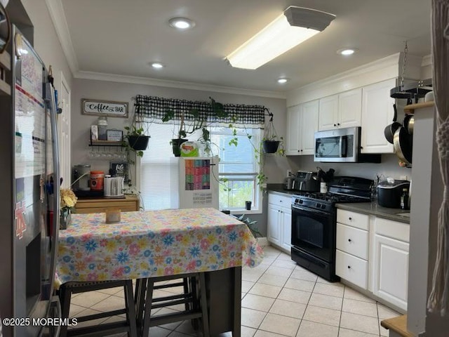 kitchen with crown molding, light tile patterned floors, black gas range oven, stainless steel microwave, and white cabinets