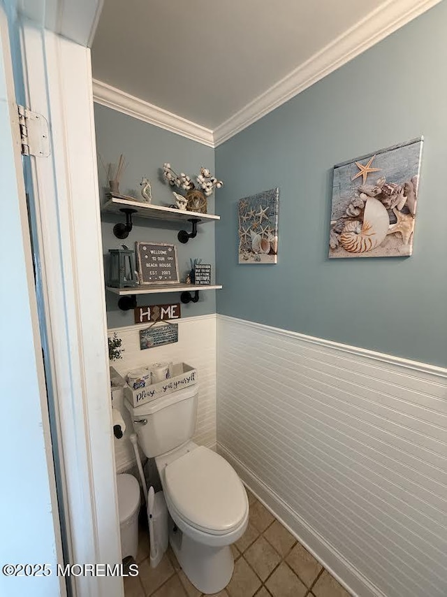 bathroom featuring crown molding, wainscoting, tile patterned floors, and toilet