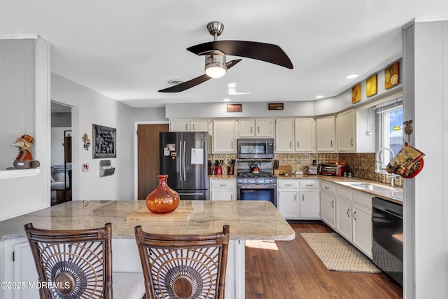 kitchen featuring a kitchen breakfast bar, backsplash, a ceiling fan, appliances with stainless steel finishes, and a sink