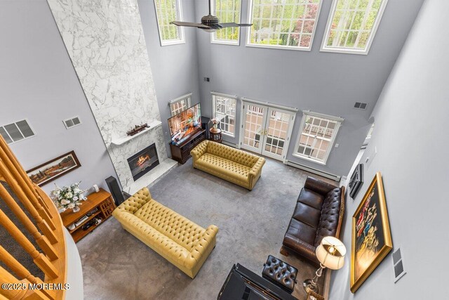 carpeted living area with visible vents, a towering ceiling, and a stone fireplace