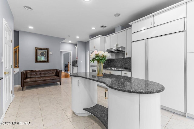 kitchen with under cabinet range hood, white cabinets, visible vents, and dark stone counters
