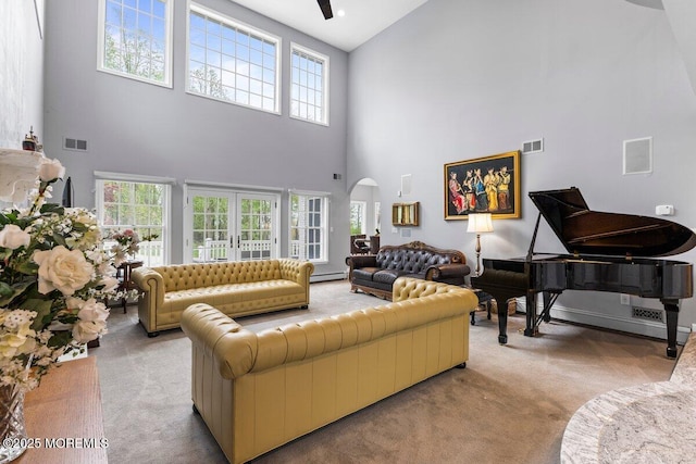 living area featuring arched walkways, visible vents, light carpet, and a towering ceiling