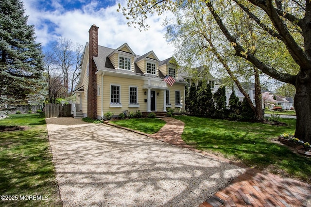 cape cod house featuring fence, a chimney, driveway, and a front yard