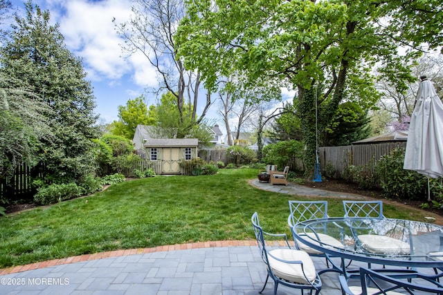 view of yard with a patio, a fenced backyard, a shed, an outbuilding, and outdoor dining space