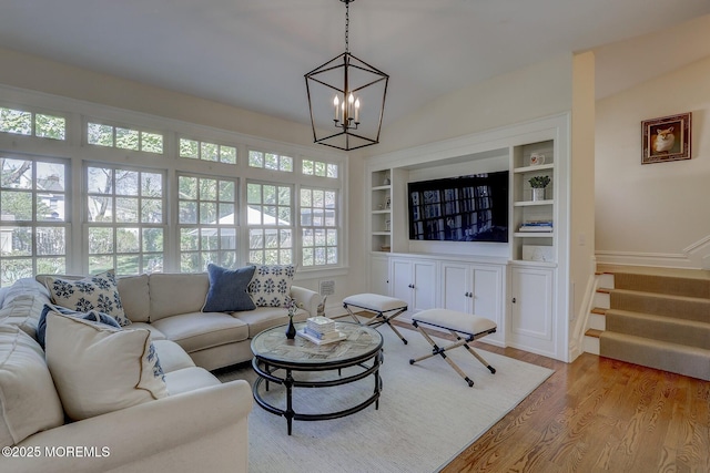 living area with built in features, wood finished floors, baseboards, an inviting chandelier, and stairs