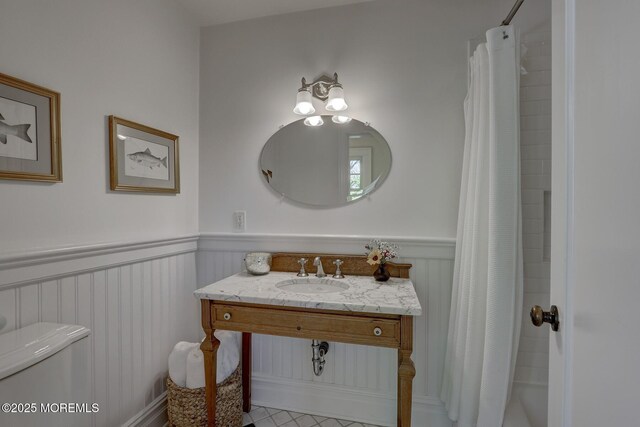 full bath featuring vanity, wainscoting, toilet, and a decorative wall
