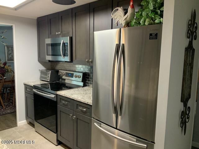 kitchen with a toaster, backsplash, appliances with stainless steel finishes, and light stone counters