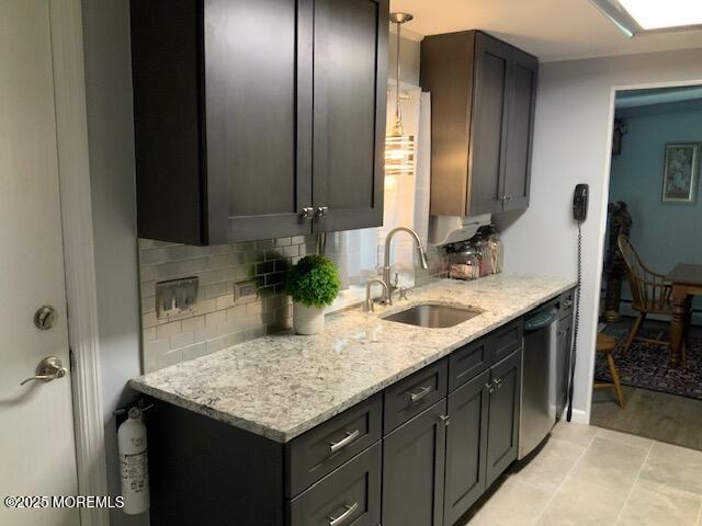 kitchen with light stone counters, decorative backsplash, stainless steel dishwasher, and a sink