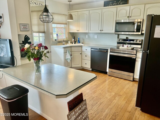 kitchen featuring hanging light fixtures, stainless steel appliances, light countertops, a sink, and light wood-type flooring