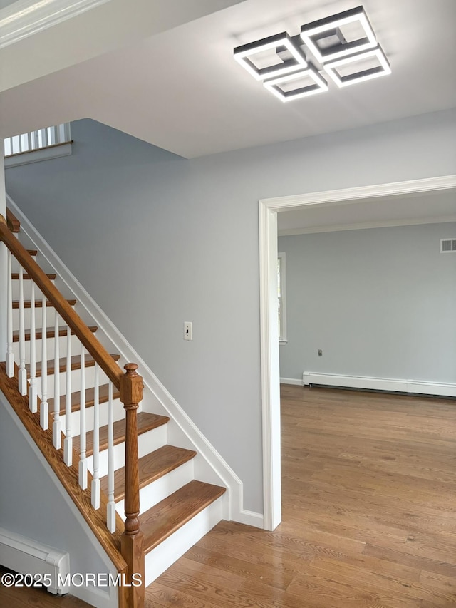 stairs with baseboards, visible vents, wood finished floors, and a baseboard radiator