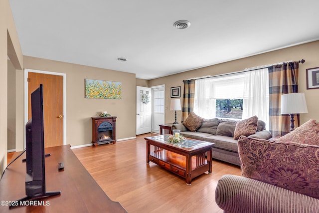 living room featuring a warm lit fireplace, visible vents, baseboards, and light wood-type flooring