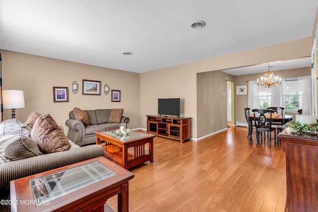 living area with an inviting chandelier, baseboards, visible vents, and light wood-type flooring