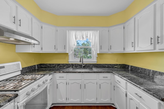 kitchen featuring white gas range, a sink, dark stone counters, under cabinet range hood, and white cabinetry