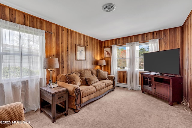 living room featuring visible vents, baseboard heating, wooden walls, and light colored carpet