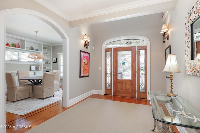 entrance foyer featuring crown molding, arched walkways, baseboards, and wood finished floors