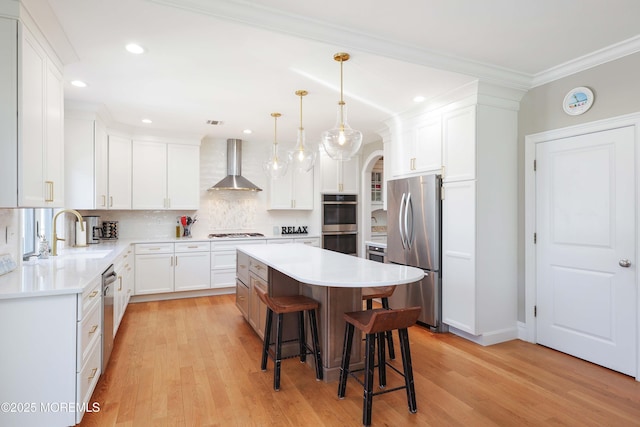 kitchen featuring wall chimney range hood, appliances with stainless steel finishes, a center island, a sink, and a breakfast bar