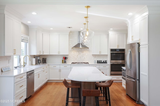 kitchen featuring a breakfast bar area, wall chimney range hood, white cabinets, a sink, and stainless steel appliances