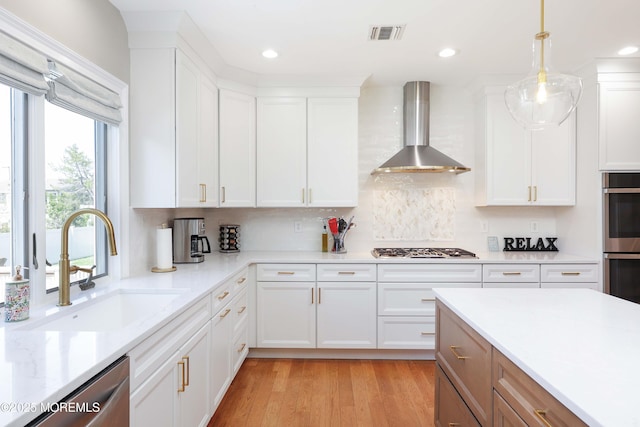 kitchen featuring wall chimney range hood, appliances with stainless steel finishes, white cabinets, and light countertops