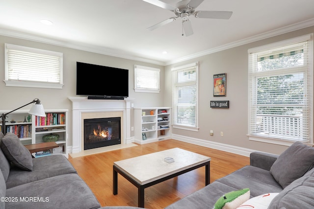 living room with crown molding, a fireplace with flush hearth, a ceiling fan, and a wealth of natural light